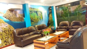 A hotel lobby with a large mural of a tropical landscape, leather sofas, and a wooden coffee table with flowers. - Paradise Hotel (Tanjung Pinang)