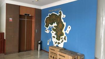 Una habitación con una pared azul que muestra un mapa de Pulau Rintan, una puerta de madera y cajas de aire acondicionado Samsung en el suelo.