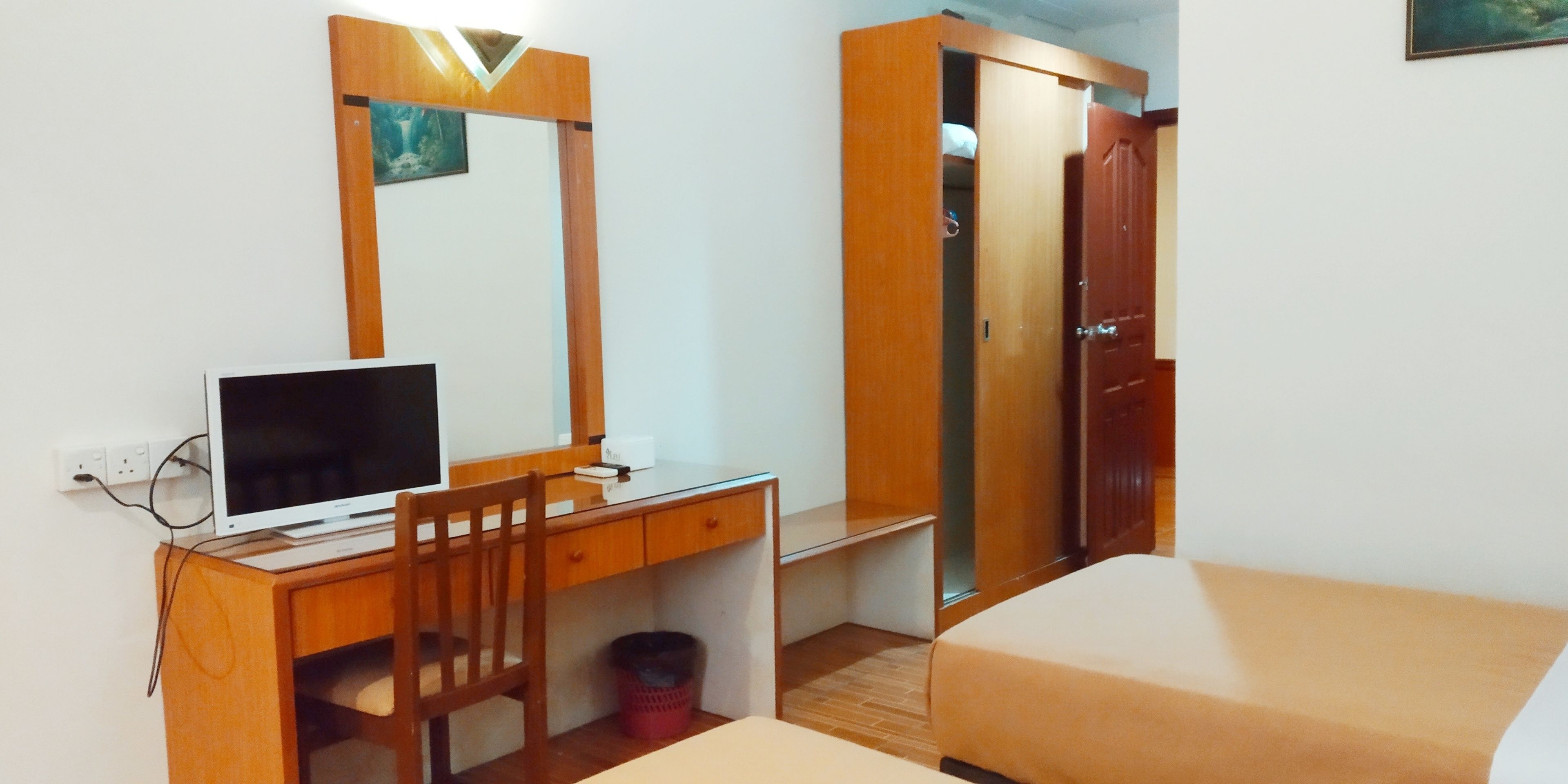 Ein Schlafzimmer mit einem Bett, einem Schreibtisch mit Computer, einem Stuhl, einem Kleiderschrank und einer kleinen Mülltonne.
