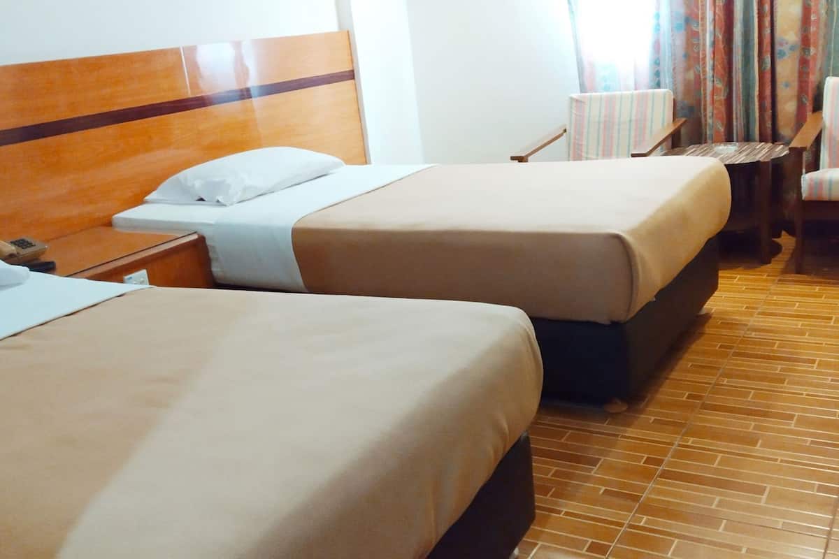 A hotel room with two beds, a nightstand, a chair, and a small table.