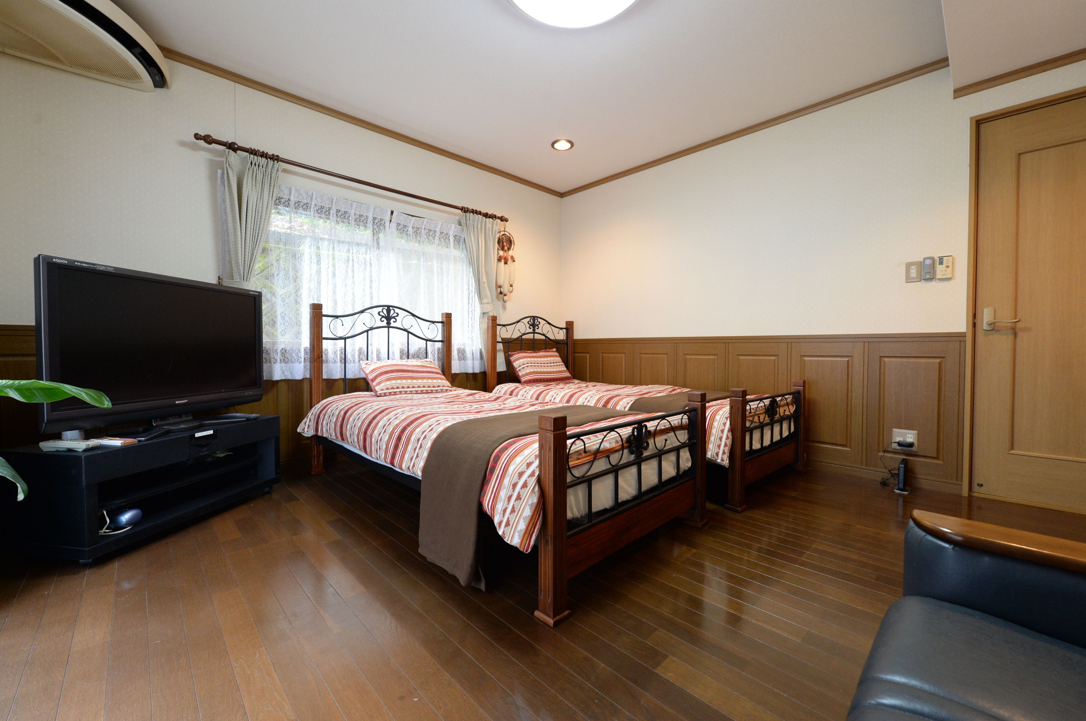 A bedroom with a bed, a TV, and a wooden floor.