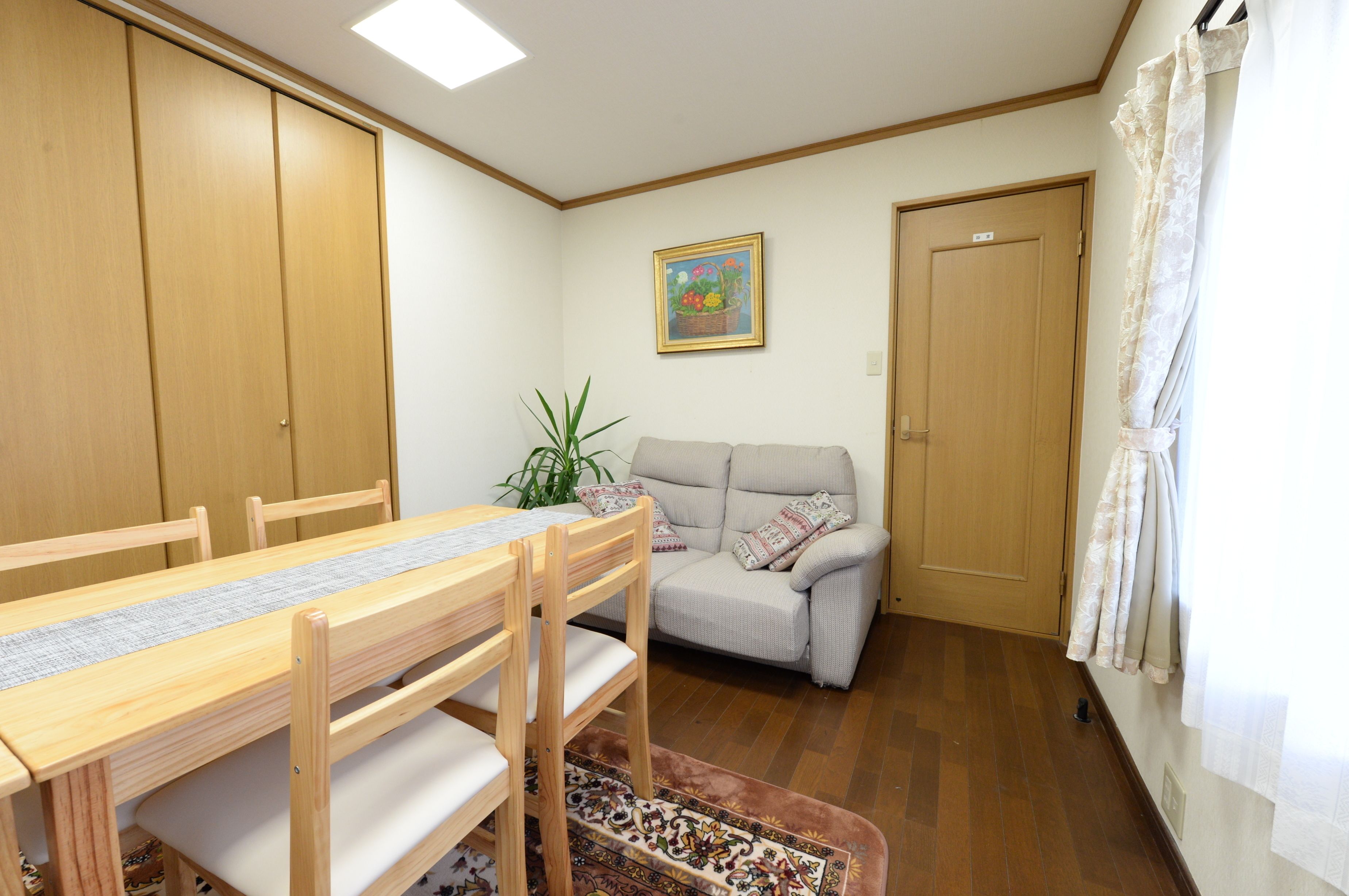 A room with a wooden dining table, a sofa, a potted plant, and a door.