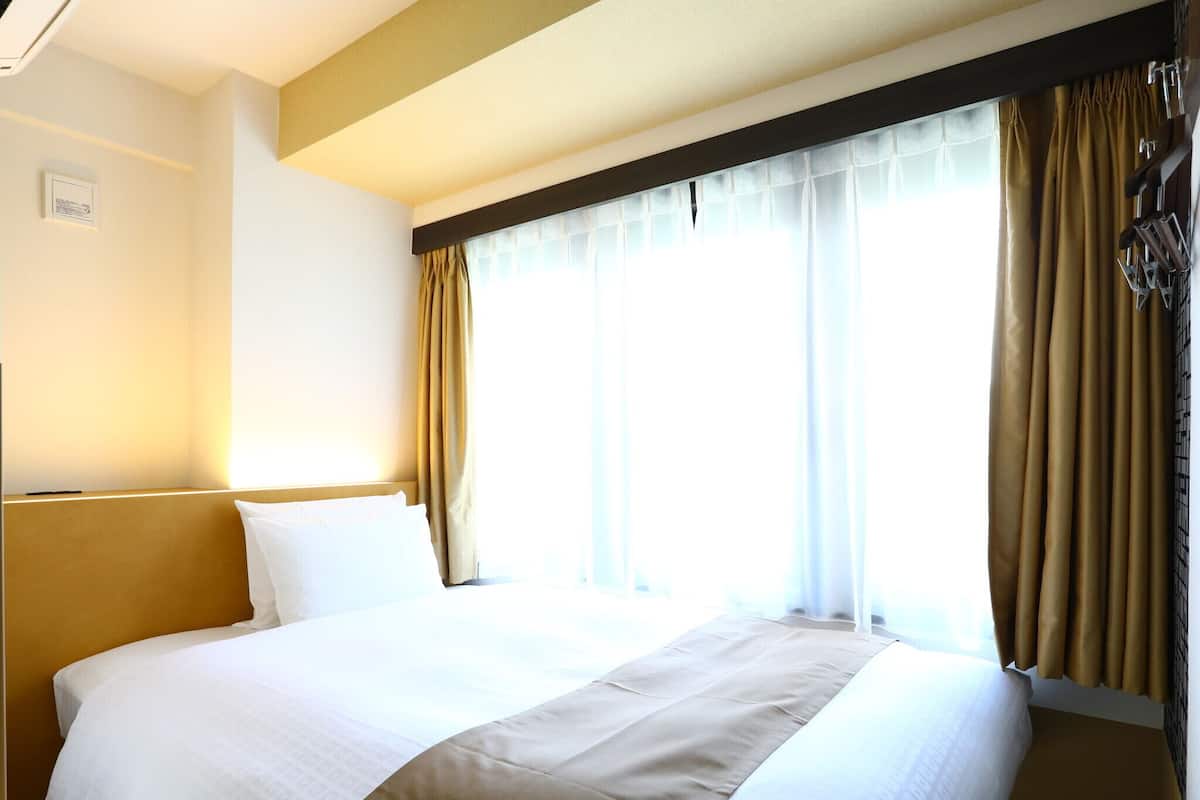 Une chambre d’hôtel avec un grand lit, des rideaux de couleur beige et une fenêtre donnant sur un beau paysage.