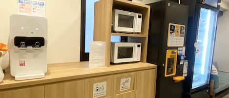 A reception desk with a water dispenser, a microwave, and a refrigerator. There are signs indicating amenities and waste disposal.