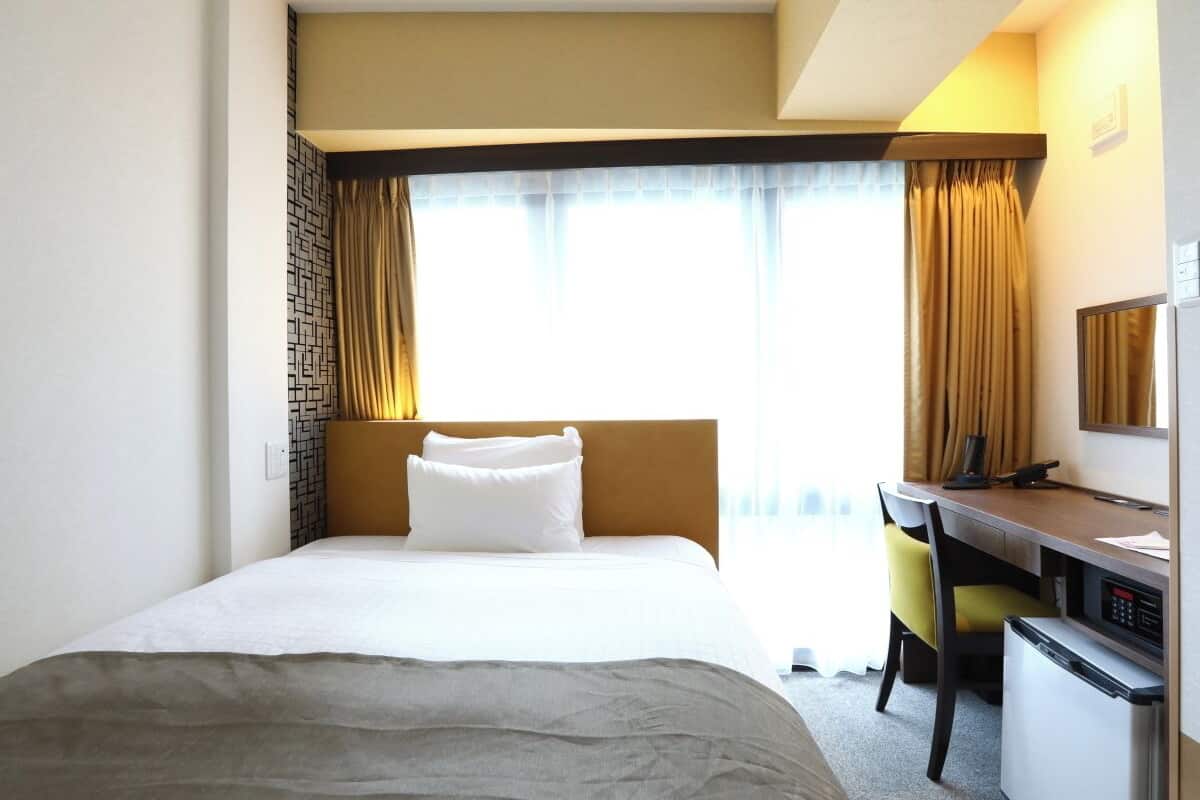 Une chambre d’hôtel avec un grand lit, un bureau, une chaise et un petit réfrigérateur.