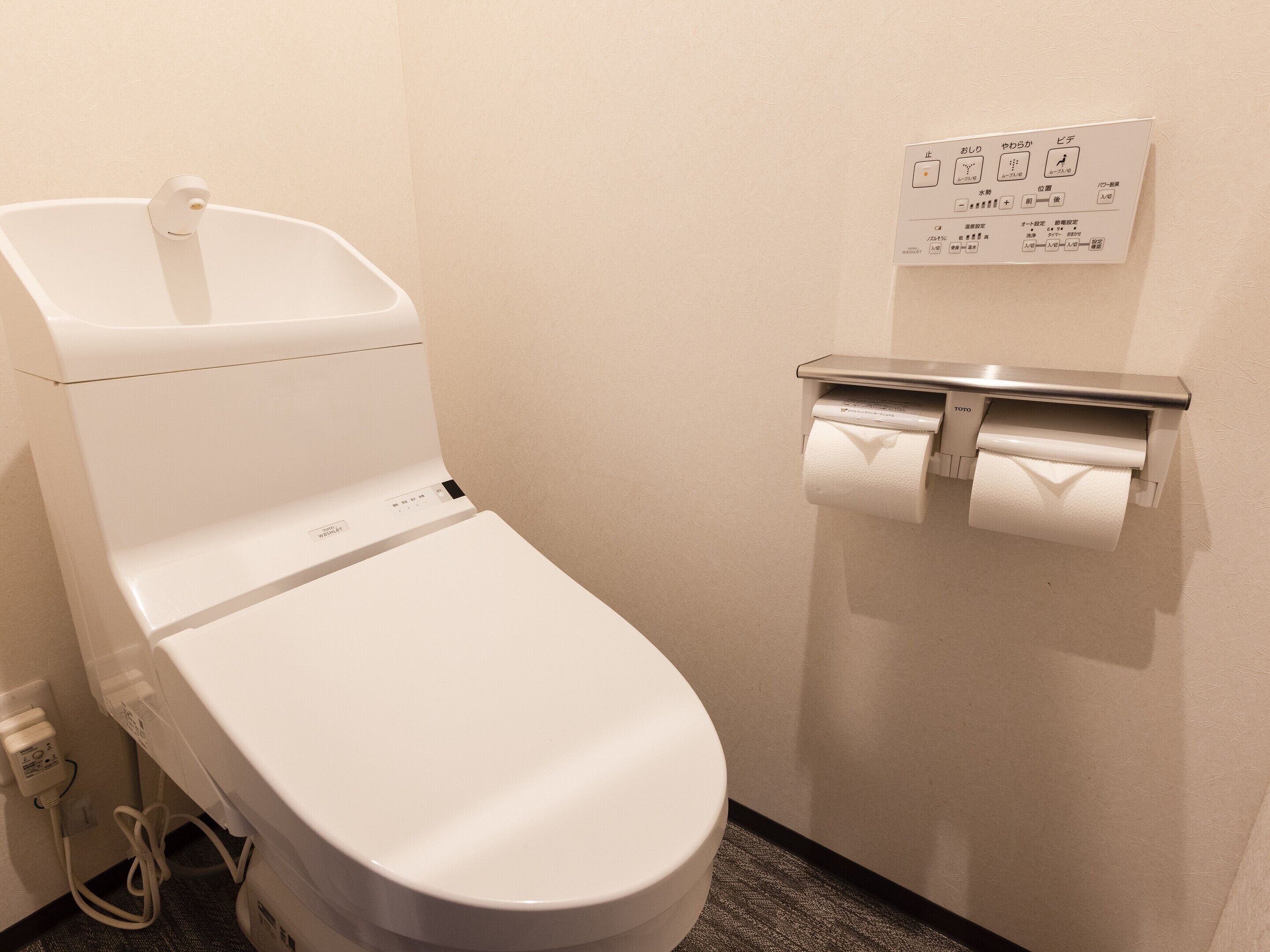 A modern toilet with a footrest, a toilet paper holder, and a control panel with Japanese instructions.