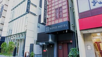 A modern hotel with a prominent entrance, glass doors, and a sign indicating it is the Koko Hotel.