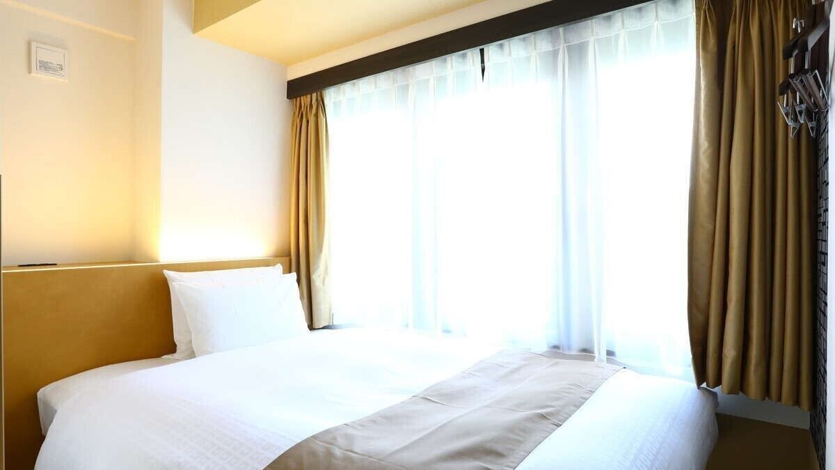 Habitación de hotel con una cama grande, cabecera y ventana con cortinas.