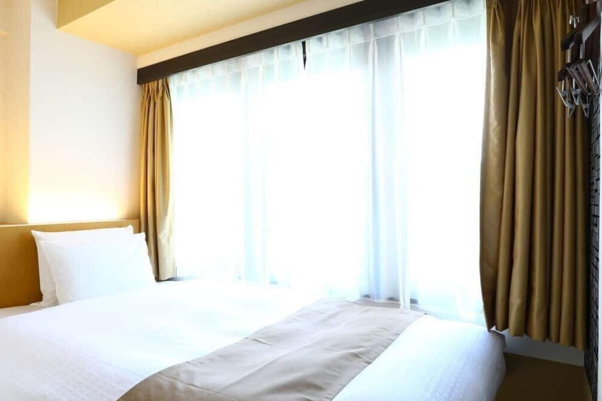 Une chambre d’hôtel avec un grand lit, une tête de lit et une fenêtre avec des rideaux.