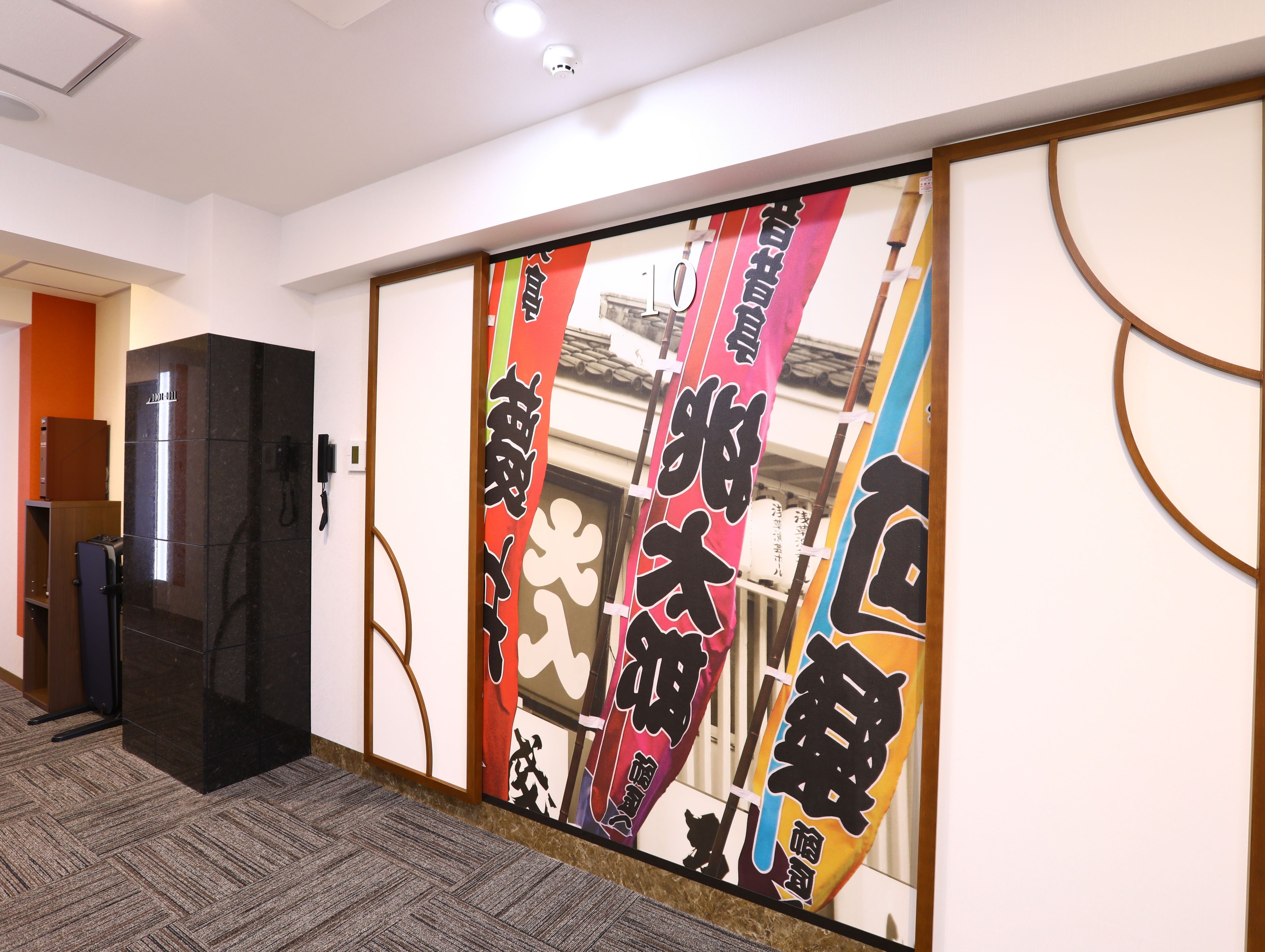 A hallway with a sliding door featuring colorful Japanese characters, a black reception desk, and a carpeted floor.