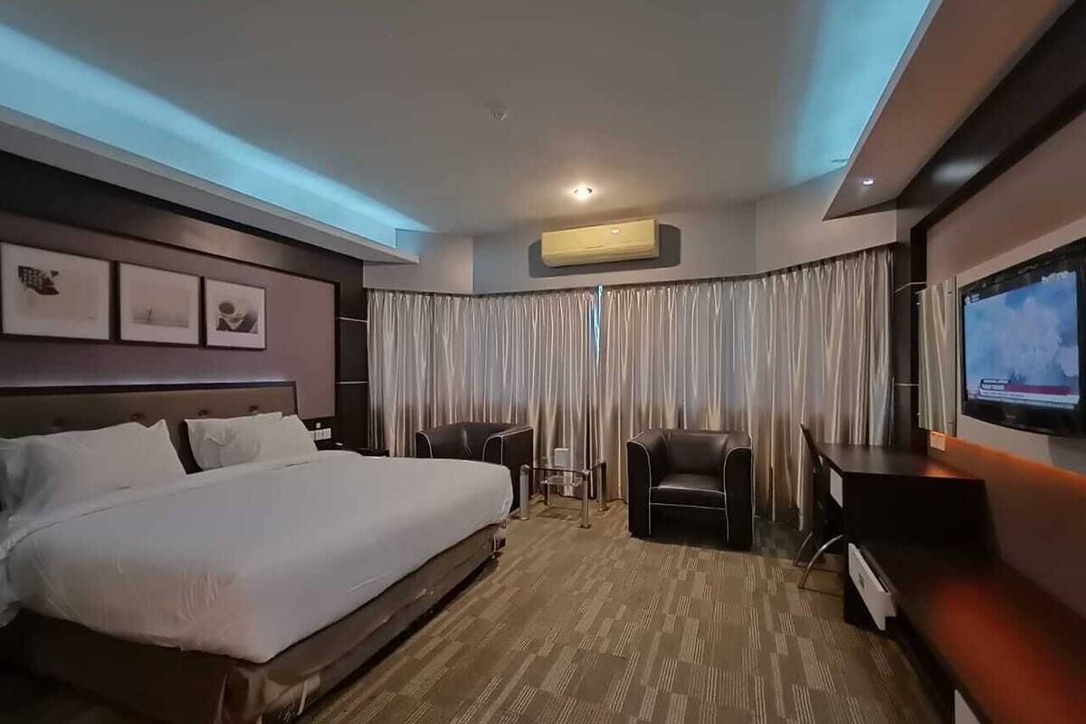 A hotel room with a large bed, a desk, a chair, a TV, and a window with curtains.