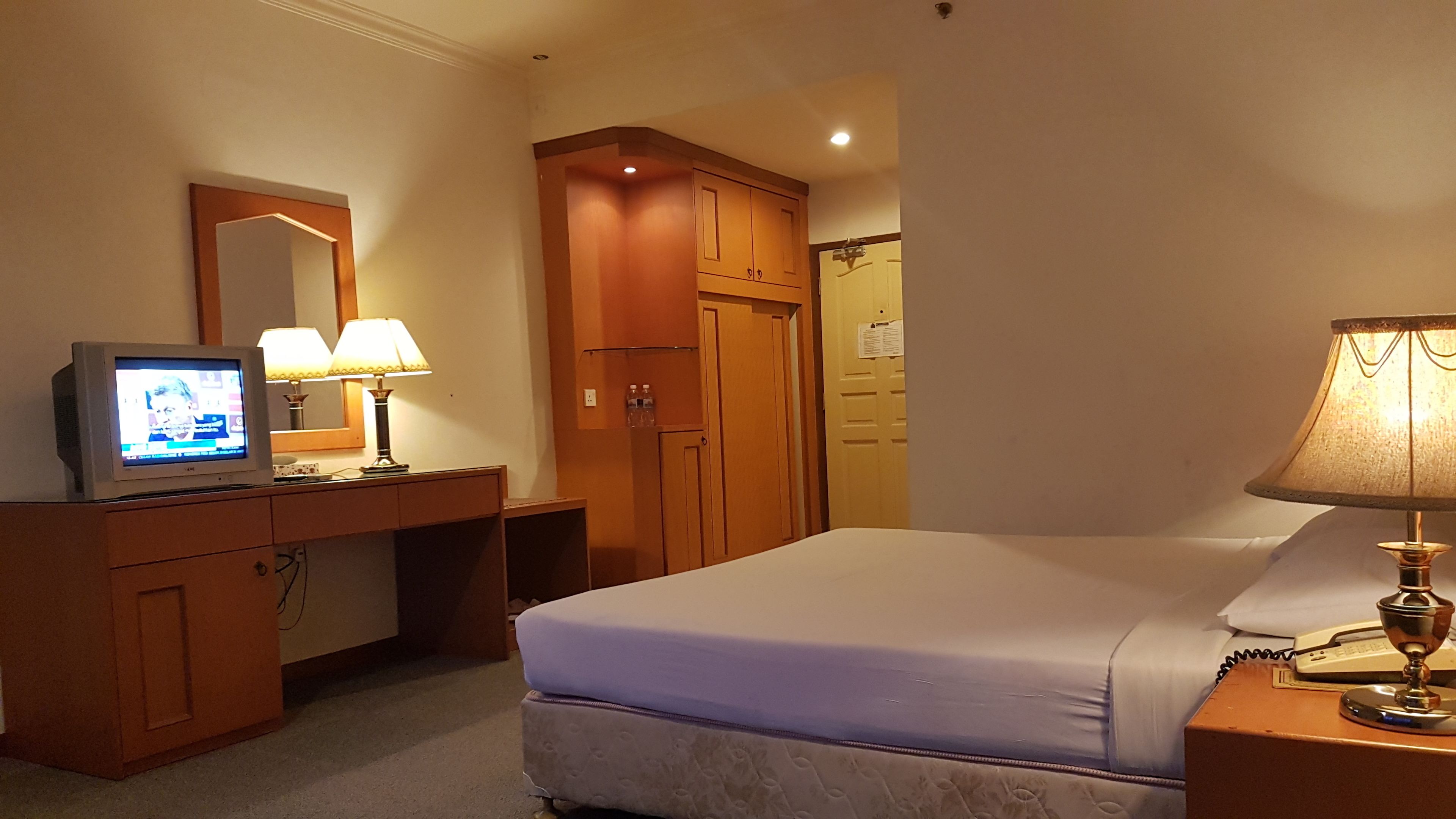 A hotel room with a bed, a desk with a television, two lamps, and a wardrobe.