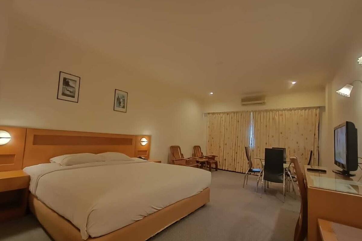 A hotel room with a large bed, a desk with a chair, a television, and two framed pictures on the wall.