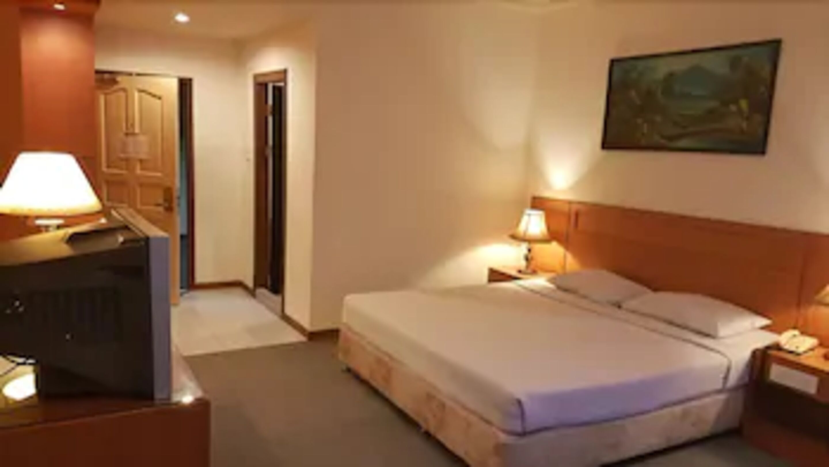 A hotel room with a bed, bedside table, lamp, and a television.