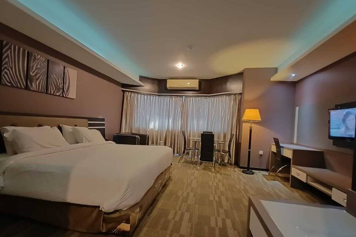 A hotel room with a large bed, a desk, a chair, a TV, and a lamp.