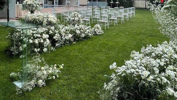 A modern building with a glass facade and a courtyard with white chairs and flowers. - Hotel Excellence Inn (Ankara)
