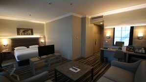 A hotel room with a bed, a TV, a desk, a chair, a sofa, and a small table. - Hotel Excellence Inn (Ankara)