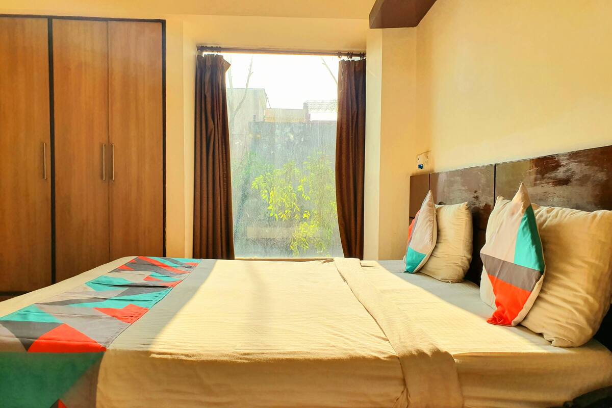 A bedroom with a bed, a window with curtains, a headboard, and a wardrobe.