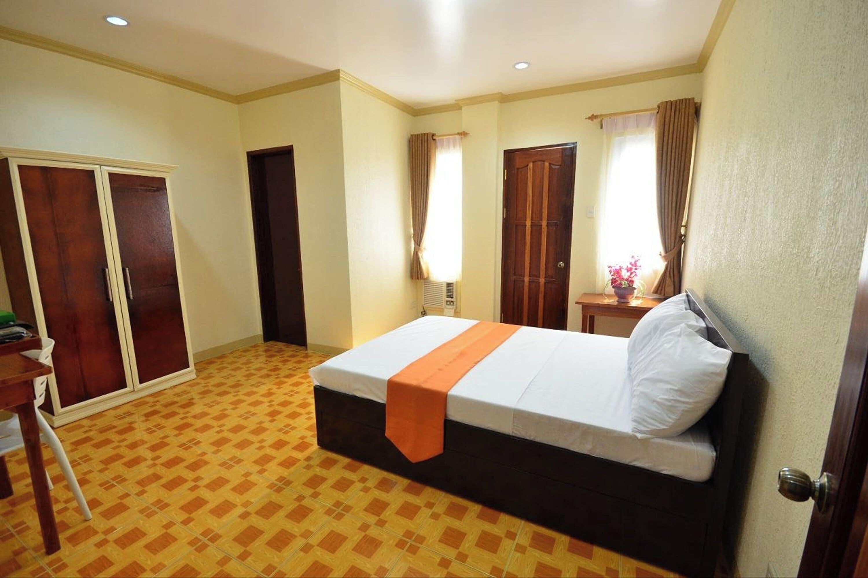 Ein Hotelzimmer mit Bett, Kleiderschrank, Schreibtisch und einem kleinen Tisch mit Blumen.