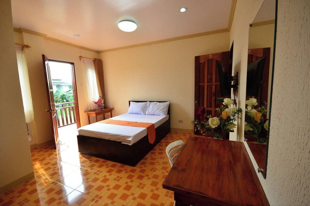 Une chambre à coucher comprenant un lit, une table en bois, une chaise, un miroir et une porte donnant sur un balcon.