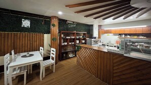 Un restaurante con interior de madera, una barra con vitrina de cristal y una zona de estar con sillas blancas y una mesa.