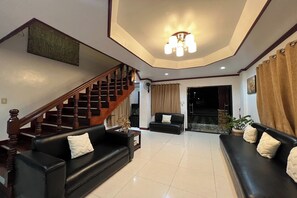 A spacious living area with a wooden staircase, black leather sofas, and a ceiling light fixture.