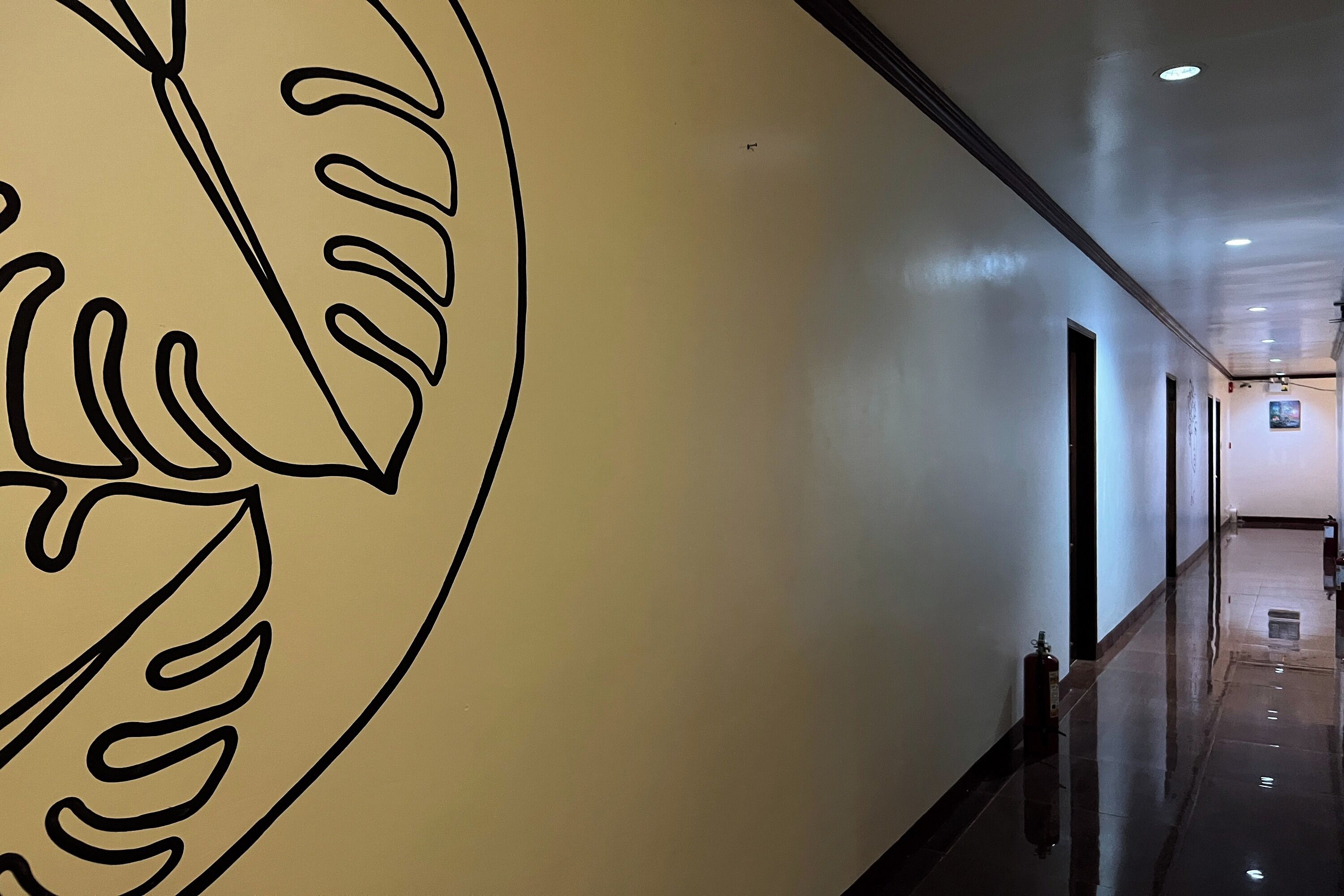 Un pasillo con un diseño de hoja grande y estilizada en la pared, piso pulido y un extintor a la vista.