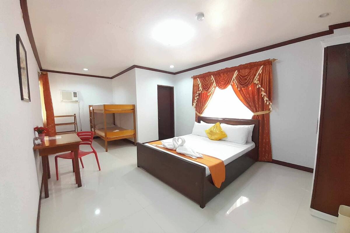 Une chambre d’hôtel comprenant un lit, un bureau avec une chaise, une armoire et une fenêtre avec des rideaux.