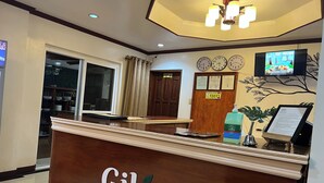 Una recepción con un letrero que dice "Gilin Suites", un reloj, un televisor y una planta en la pared.