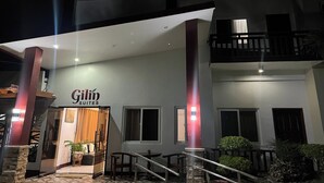 Entrada de un hotel con un cartel que dice "Gilín Suites", una escalera y un balcón con barandillas.