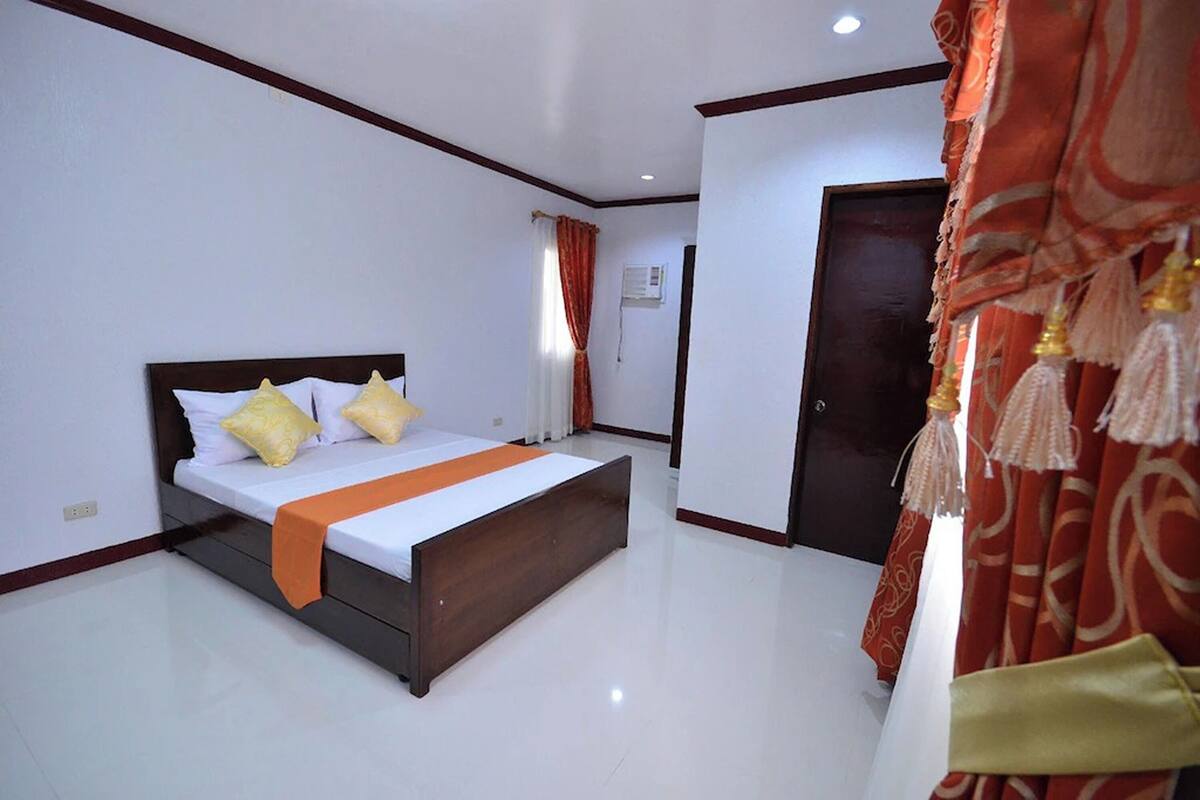 Une chambre à coucher avec un lit, des murs blancs, une tête de lit en bois et un rideau rouge.