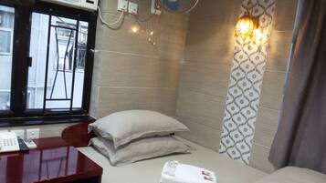 A hotel room with a bed, a desk with a telephone, a wall-mounted fan, and a window with a view of the outside.