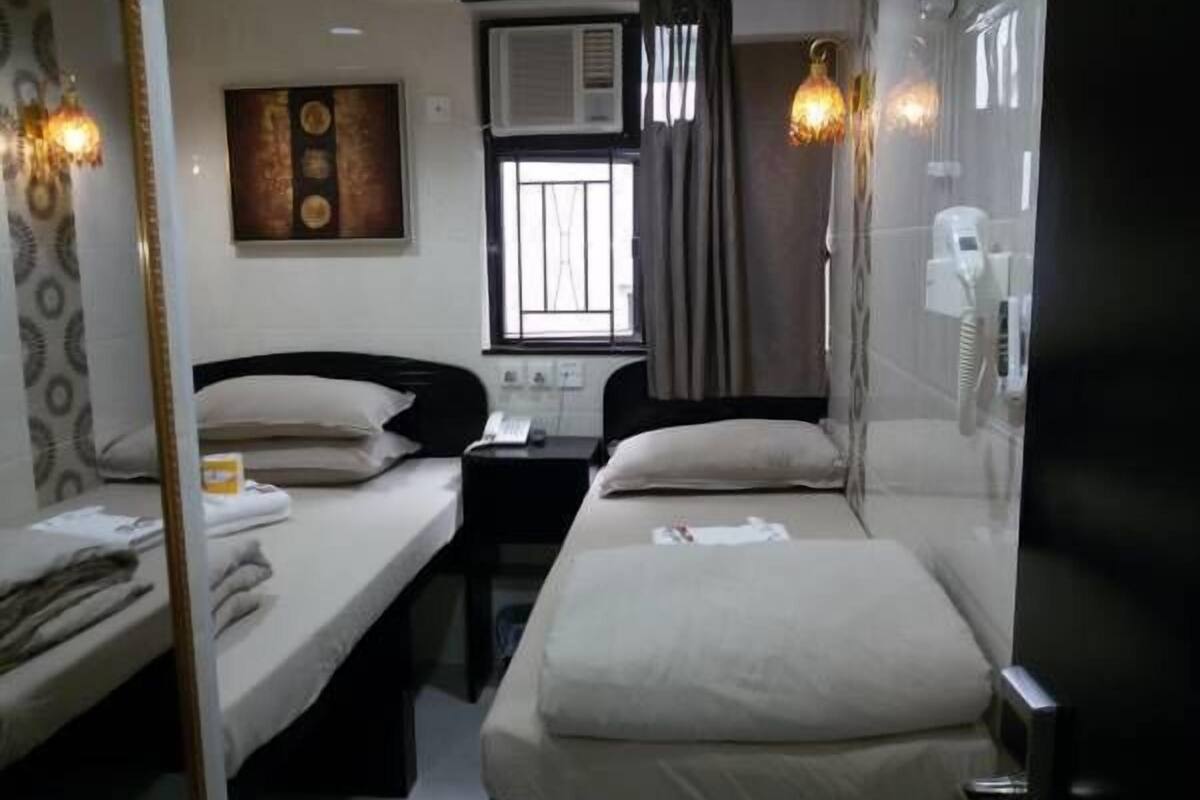 A hotel room with two single beds, a desk, a chair, a mirror, and a window with curtains.