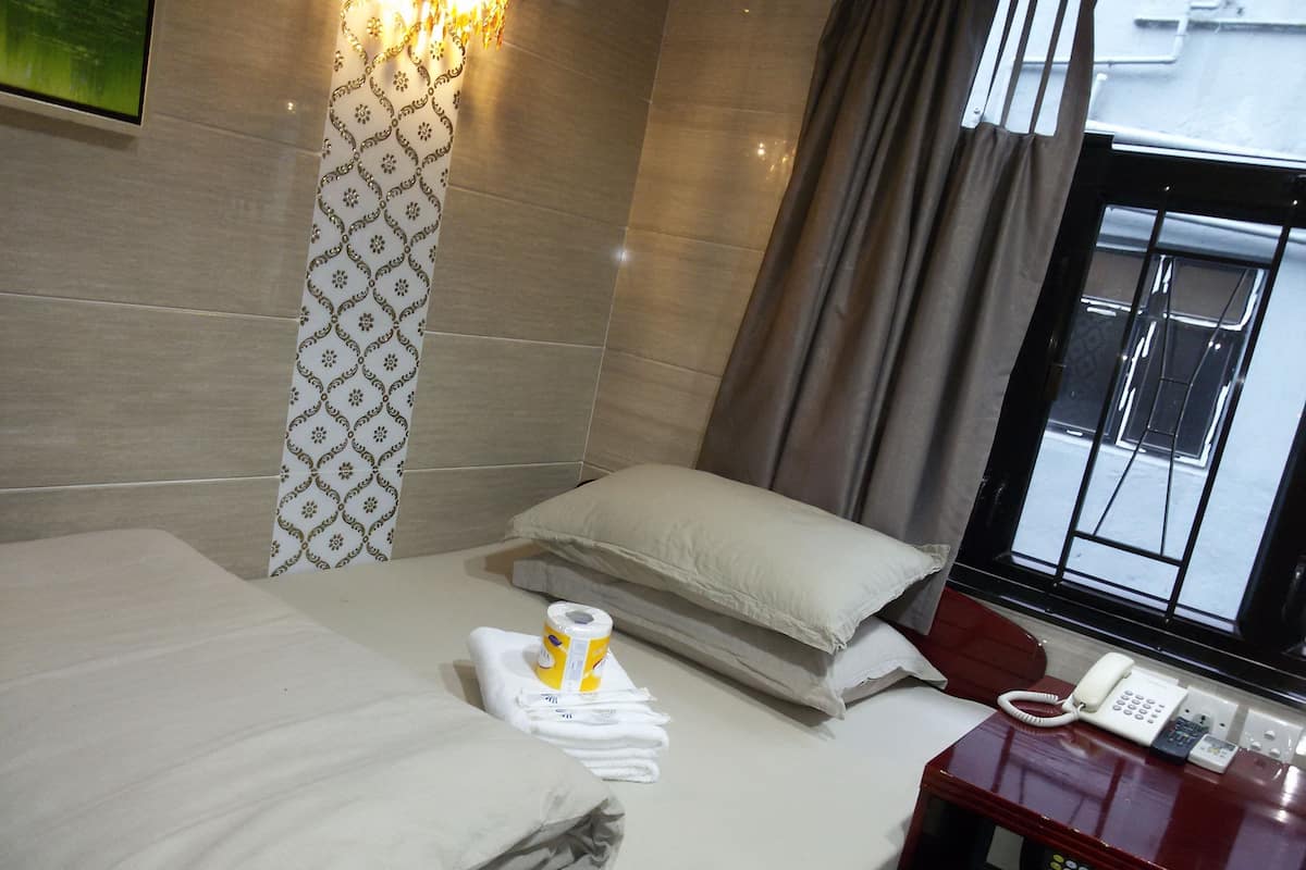 A hotel room with a bed, a bedside telephone, a window with curtains, and a wall-mounted light fixture.