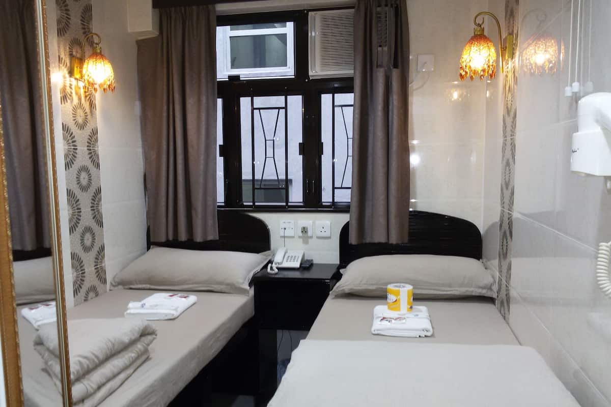 A compact hotel room with two single beds, a small desk with a telephone, and a window with curtains.