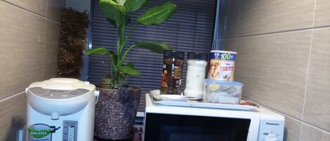 A compact kitchen with a microwave, a rice cooker, and a potted plant.
