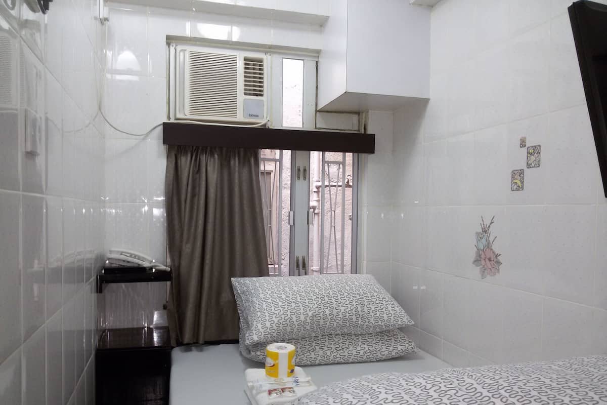 A small, clean room with a bed, a window with curtains, a radiator, and a wall with a small decorative item.