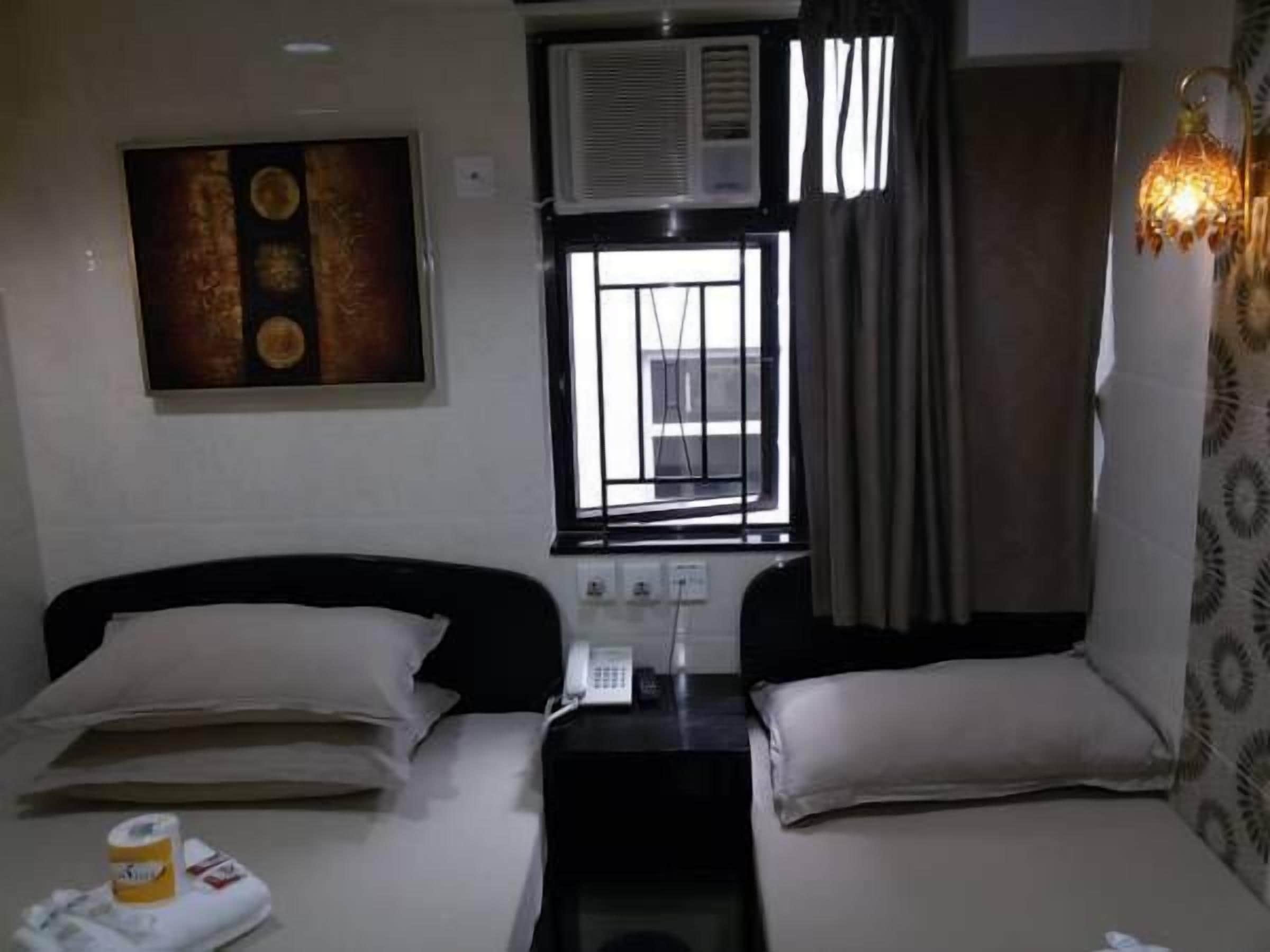 Une chambre d’hôtel avec deux lits, un tableau au mur, un climatiseur, un téléphone et un rideau à motifs.