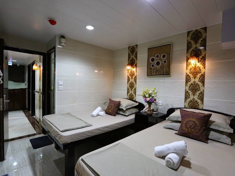 A hotel room with two beds, a bedside table, a wall-mounted lamp, and a door leading to another room.