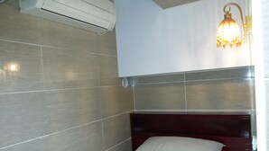 A small, compact bathroom with a shower area, a bed with pillows, and a wall-mounted air conditioning unit. - Asia Inn (Kowloon)