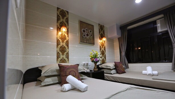 A hotel room with two beds, each with a rolled towel, a vase with flowers, and decorative pillows. - Asia Inn (Kowloon)