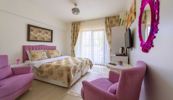 A bedroom with a bed, two pink chairs, a bedside table, a mirror, and a television. - Sahra Butik Hotel (Sapanca)