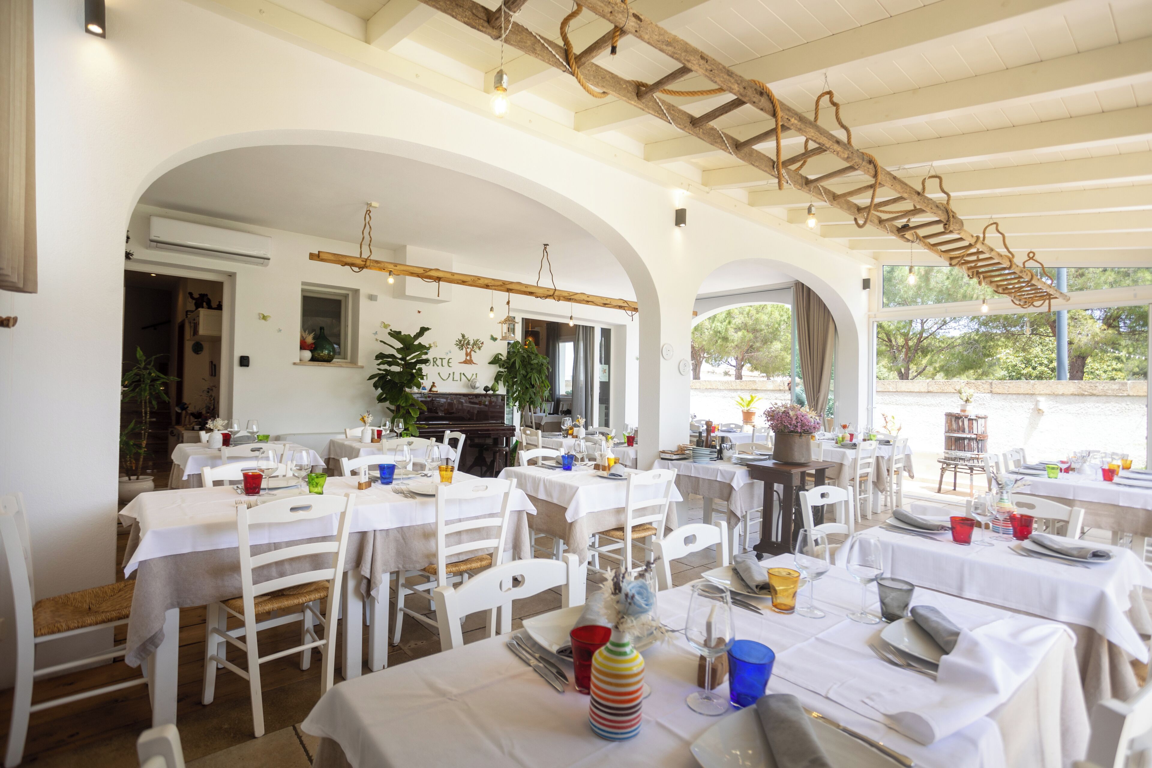 Un espace repas avec des tables et des chaises blanches, un plafond en bois et une lumière naturelle provenant de grandes fenêtres.