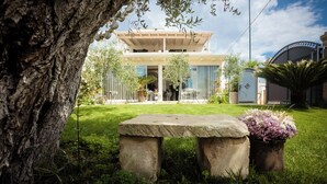 Una casa moderna con un balcone, una panca in pietra e piante in vaso in un giardino.