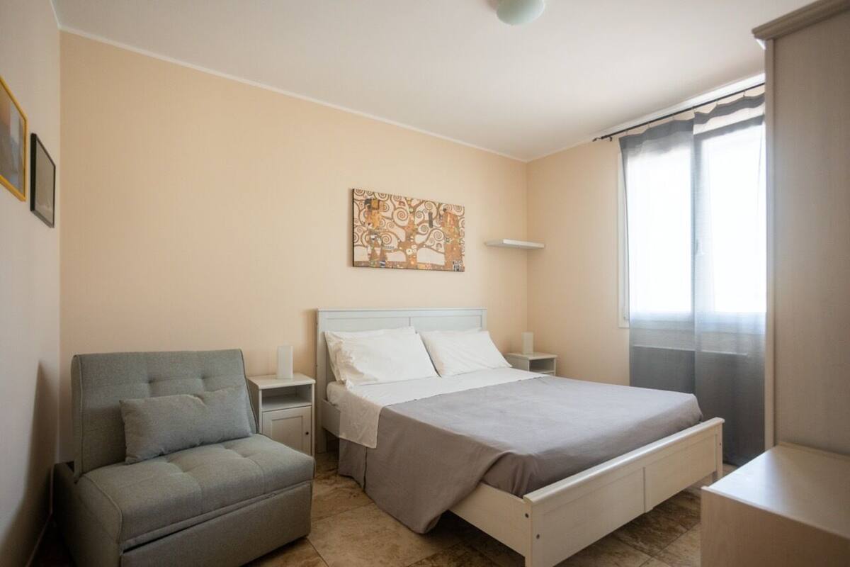 A bedroom with a bed, a nightstand, a chair, and a painting on the wall.