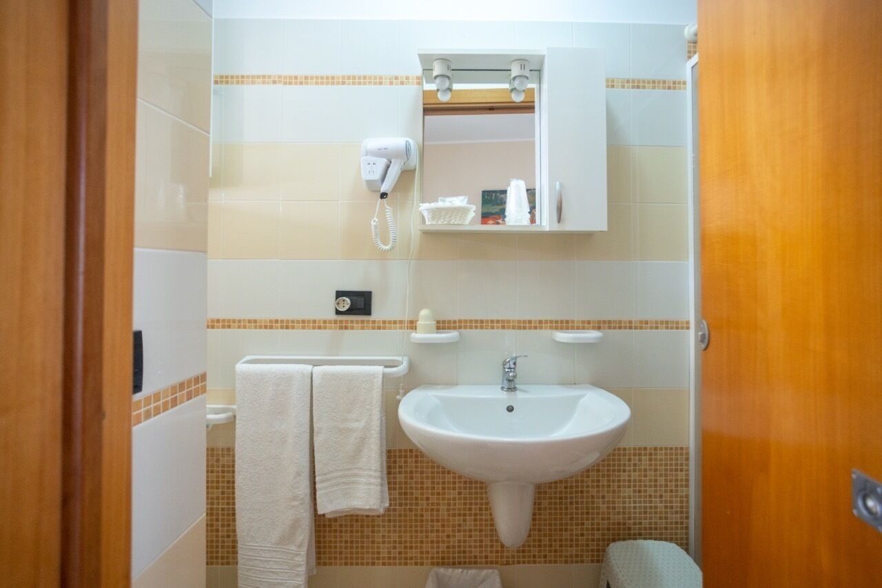 Un baño con lavamanos blanco, toallero con dos toallas, secador de pelo y espejo sobre el lavamanos.