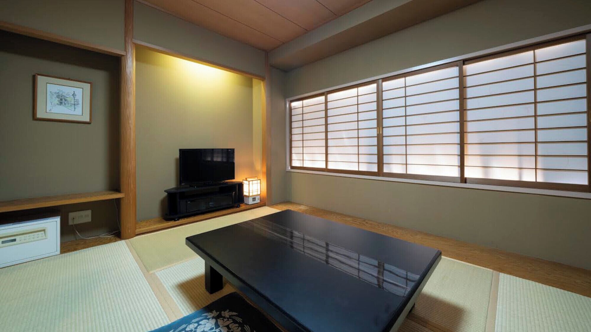 Una habitació japonesa tradicional amb tatami, una taula negra, una televisió i un panell shoji.
