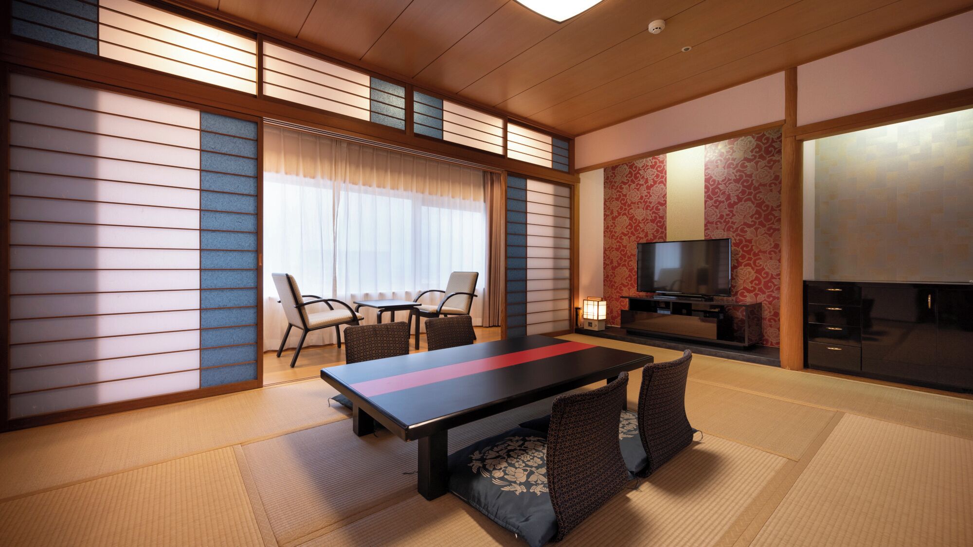 Habitació d'estil japonès tradicional amb sòl de tatami, una taula baixa amb coixins, un televisor i una porta corredissa.