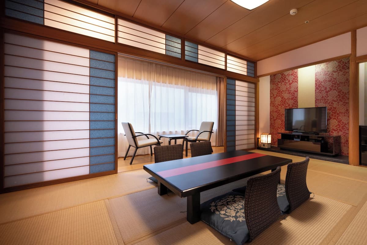 Una habitación tradicional japonesa con suelo de tatami, una mesa baja con cojines, televisor y puerta corredera.