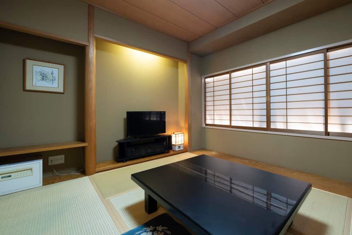 Ein traditioneller japanischer Raum mit Tatami-Boden, einem niedrigen Tisch, einem Fernseher und einem Shoji-Bildschirm.